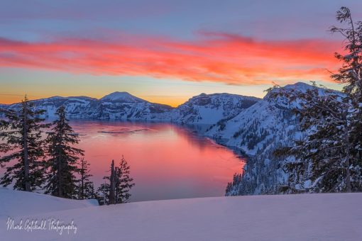 Crater Lake Sunrise; the sunrise lights up the clouds and reflects off the lake.