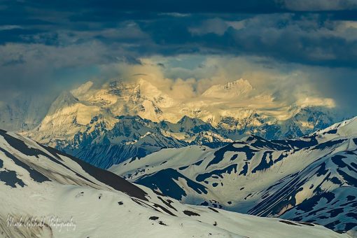 Snowy mountains spot lighted by the sun under dramatic clouds